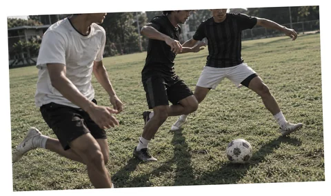 Dua pemain berebut bola di padang rumput