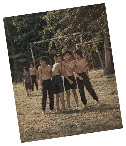 Sekumpulan budak lelaki berdiri di depan gol buatan sendiri di padang kampung