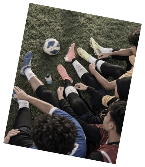 Sekumpulan pemain duduk di atas rumput dengan kasut dan sebiji bola di tengah
